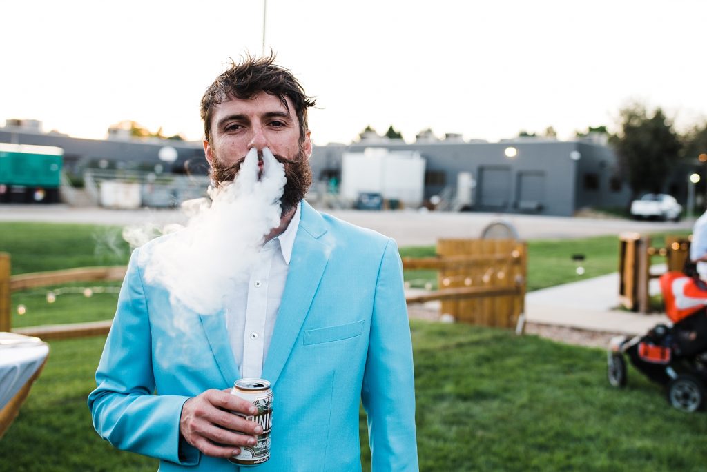 man in blue suit blowing cigar smoke out nostrils