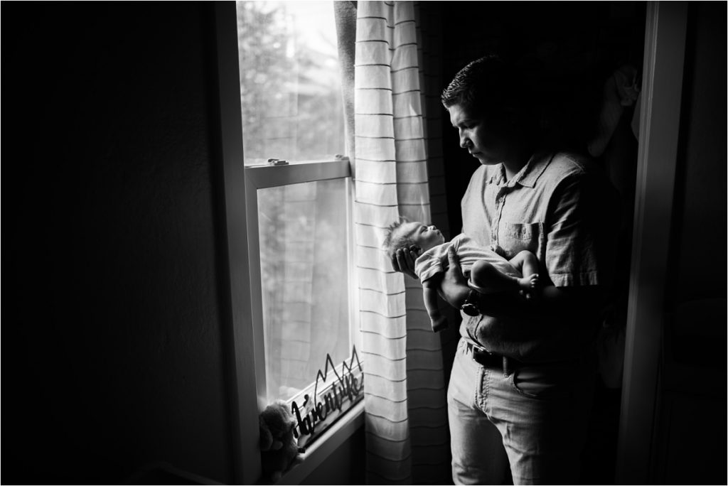 dad holding newborn baby near window