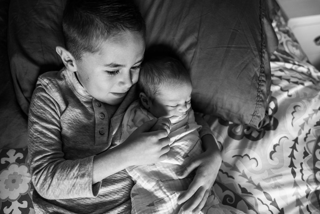 Boy snuggling with newborn baby brother.