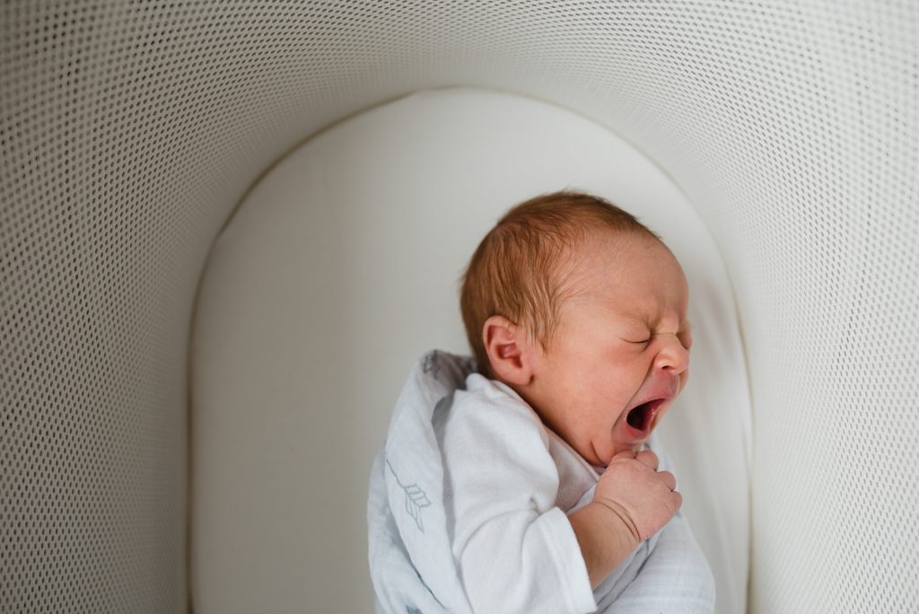 Baby yawning in bassinet.