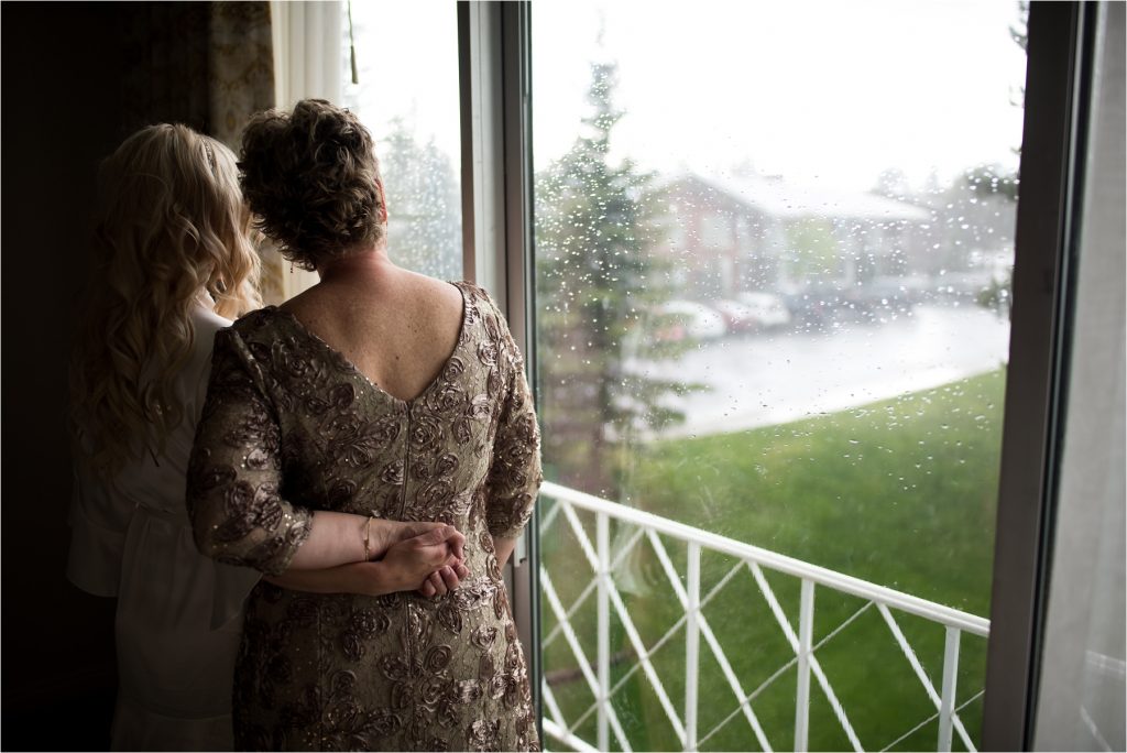 Bride and mom looking out rainy window, photographed on Nikon 28 1.4.