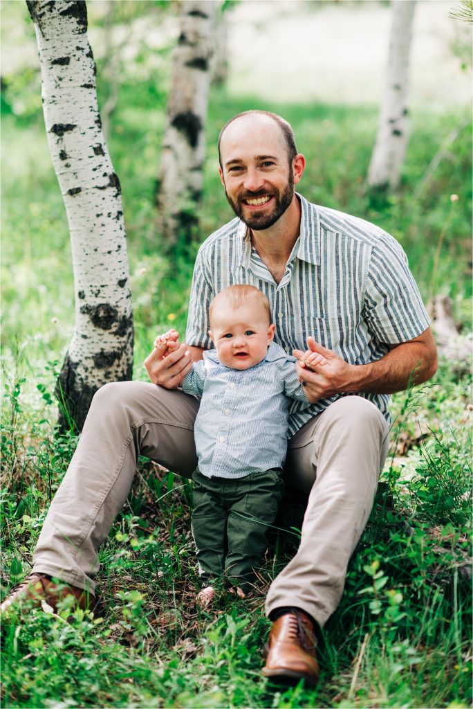 Dad holding baby while sitting on log during six month old photoshoot.