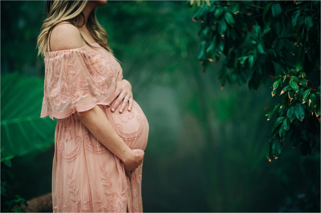 Woman holding pregnant belly near green trees in fog