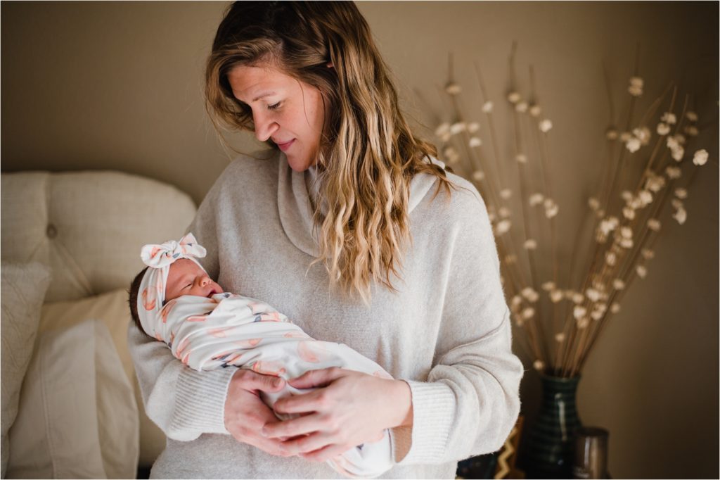 New mom in cream sweater, holding baby wrapped in cream and coral swaddle.