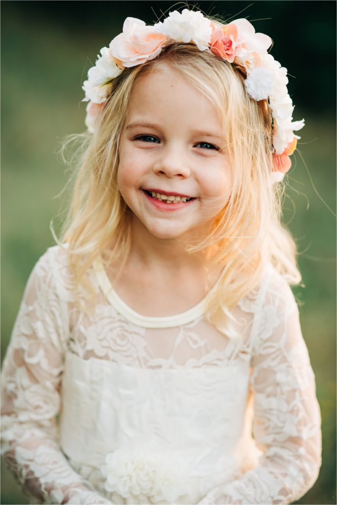 Girl smiling at camera while wearing white dress and flower crown.