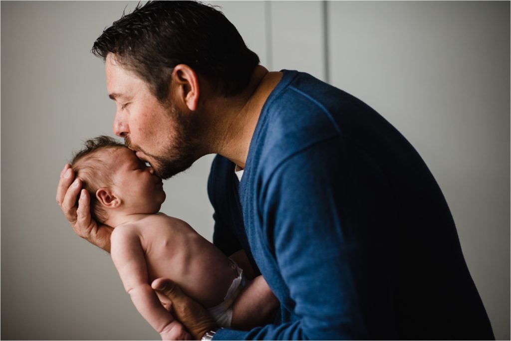 Dad kissing newborn daughter on forehead.