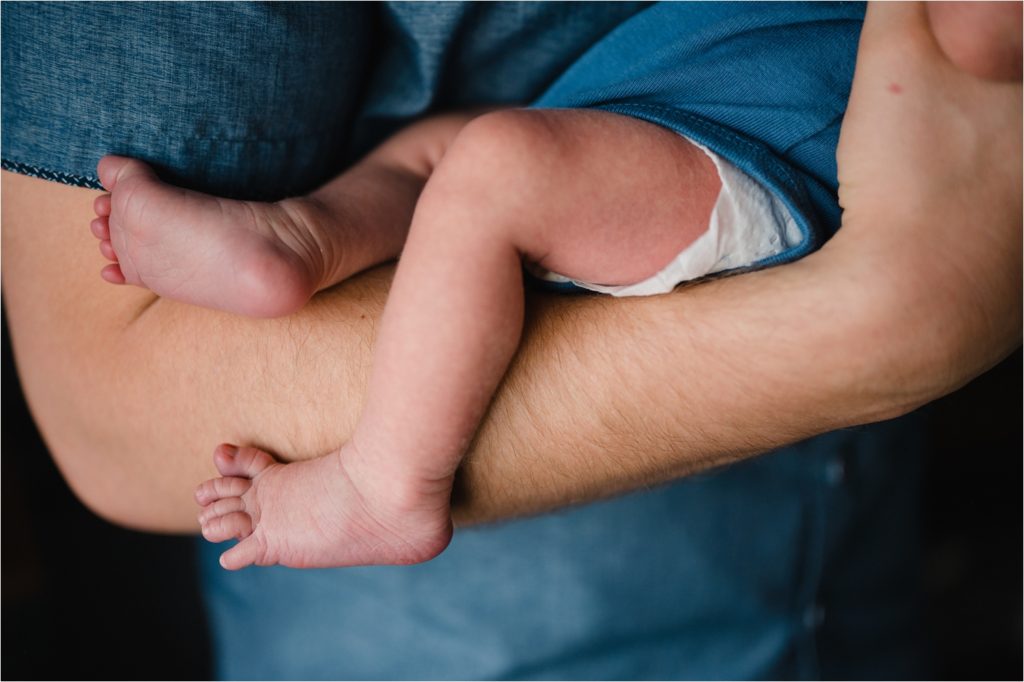 Newborn baby legs drooping over dad's arms.