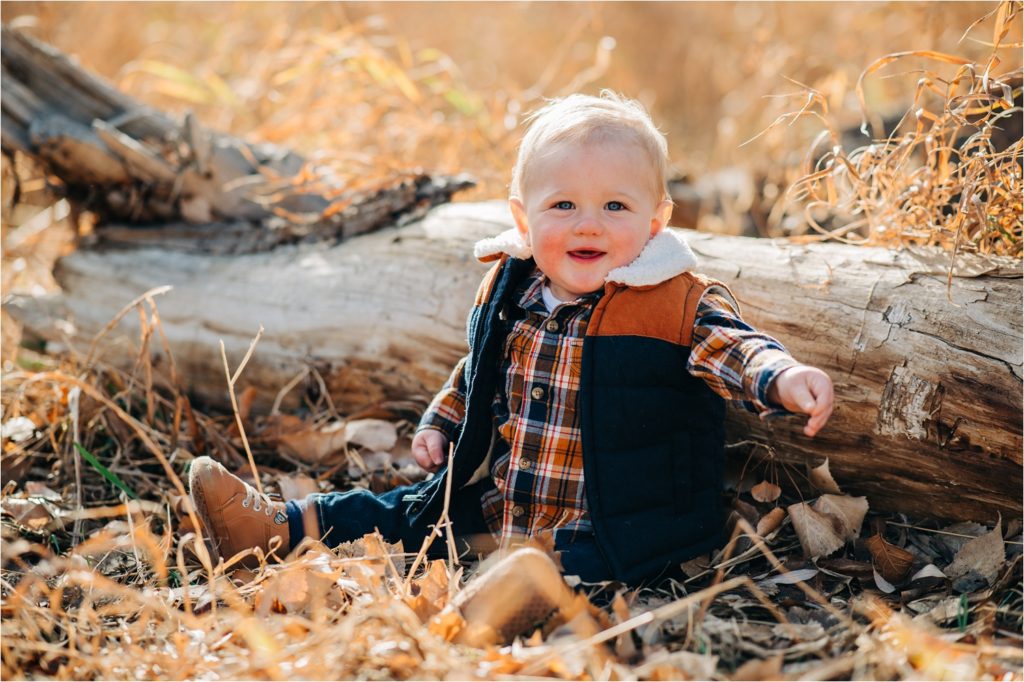 Little boy leaning against log and smiling.