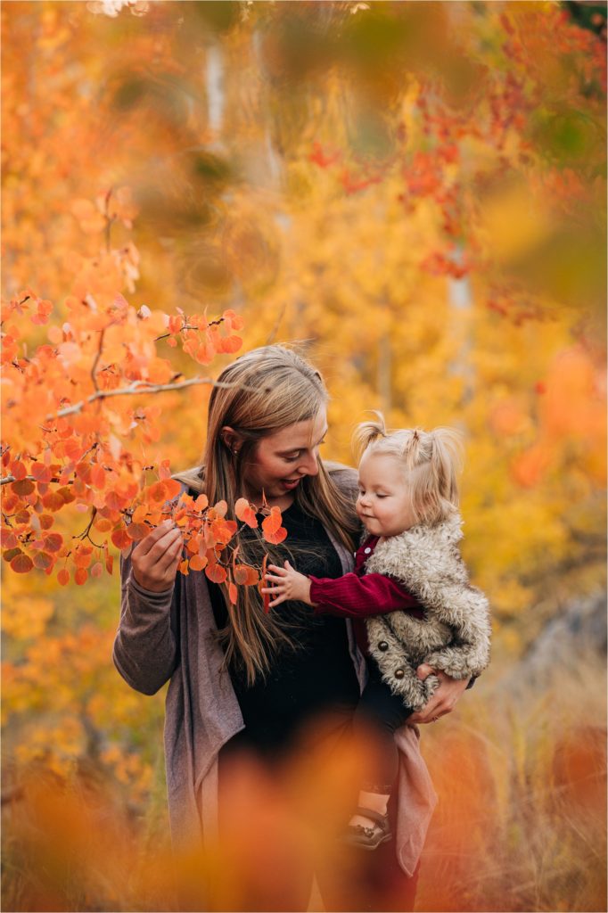Mom and daughter in orange aspen leaves.