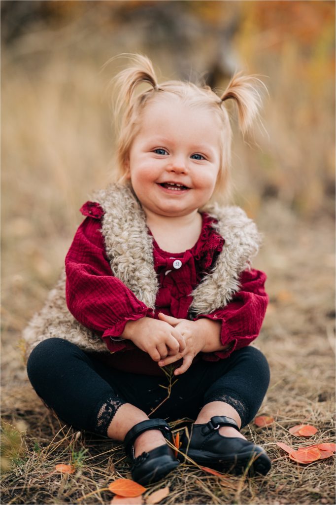 Little girl with pigtails sitting and laughing in dirt during Wyoming mountain session.