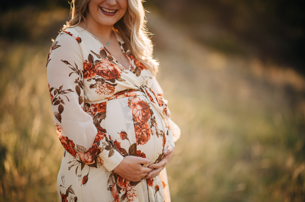 Woman laughs while holding pregnant belly.
