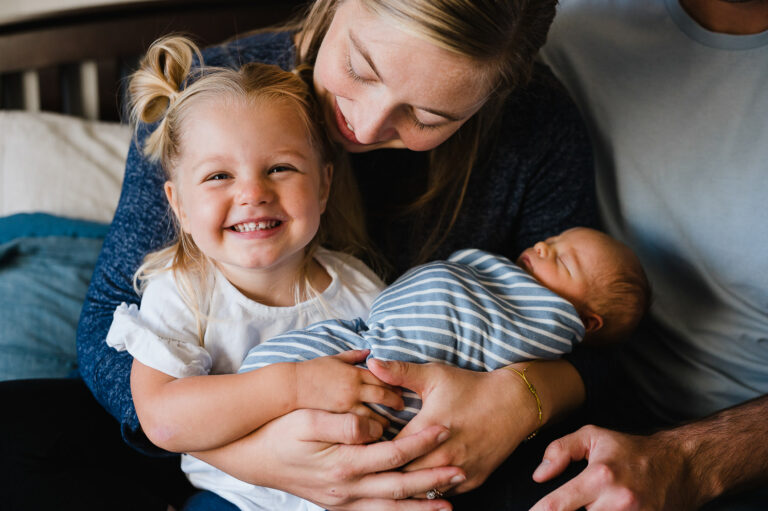 Toddler smiles while holding new baby brother.