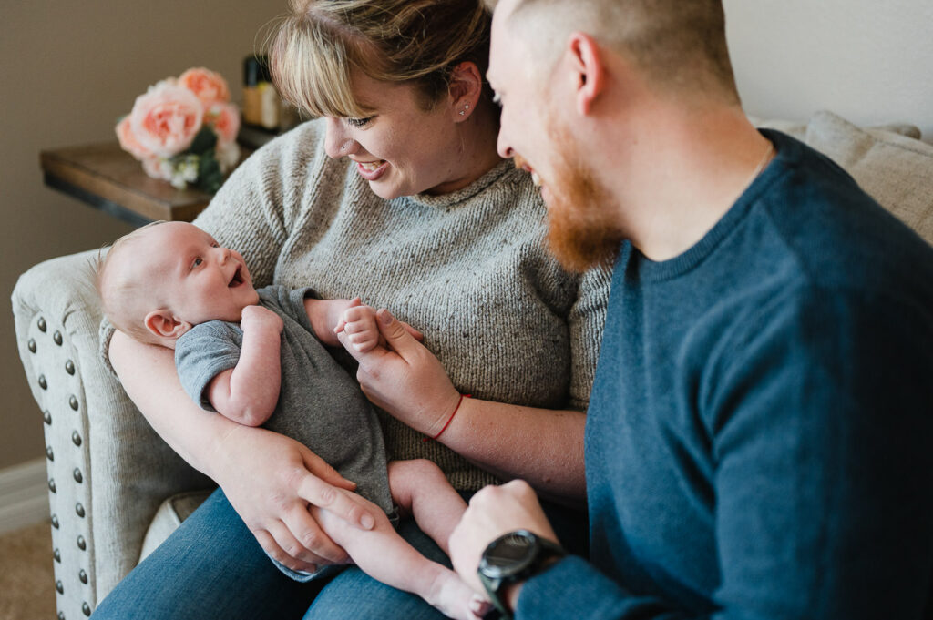 Mom in gray sweater and dad in blue sweater holding smiling baby boy in gray onesie.