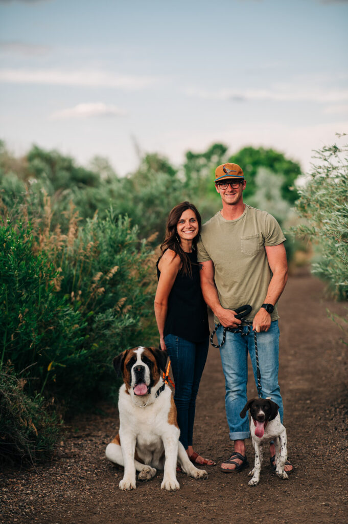 Couple holds the leashes of a St Bernard and a German Shorthair Pointer, while standing near the Willows at Riverbend Ponds Natural Area in Fort Collins.