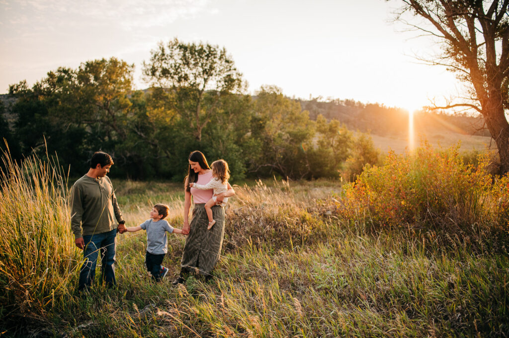Wyoming family of four stands in tall grass near tall cottonwoods, while the sun sets behind the hill.