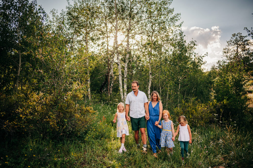 Family of five walks through tall grass near aspen grove in Wyoming.
