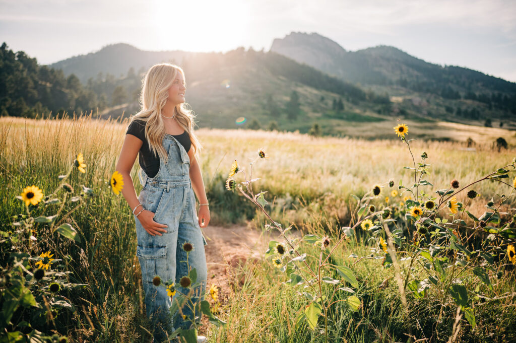 High school girl in denim overalls stands in a field of sunflowers at Lory State Park.